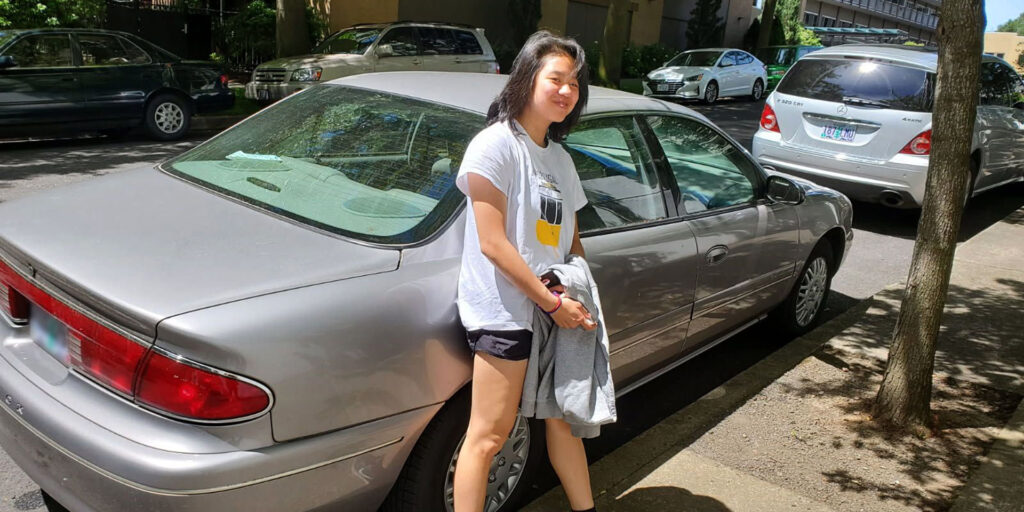 Teen Lilly stands in front of her grandma's silver Buick.